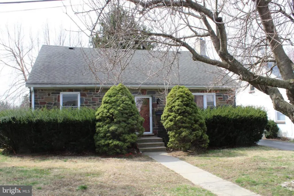 Stone bungalow with evergreen shrubs and walkway