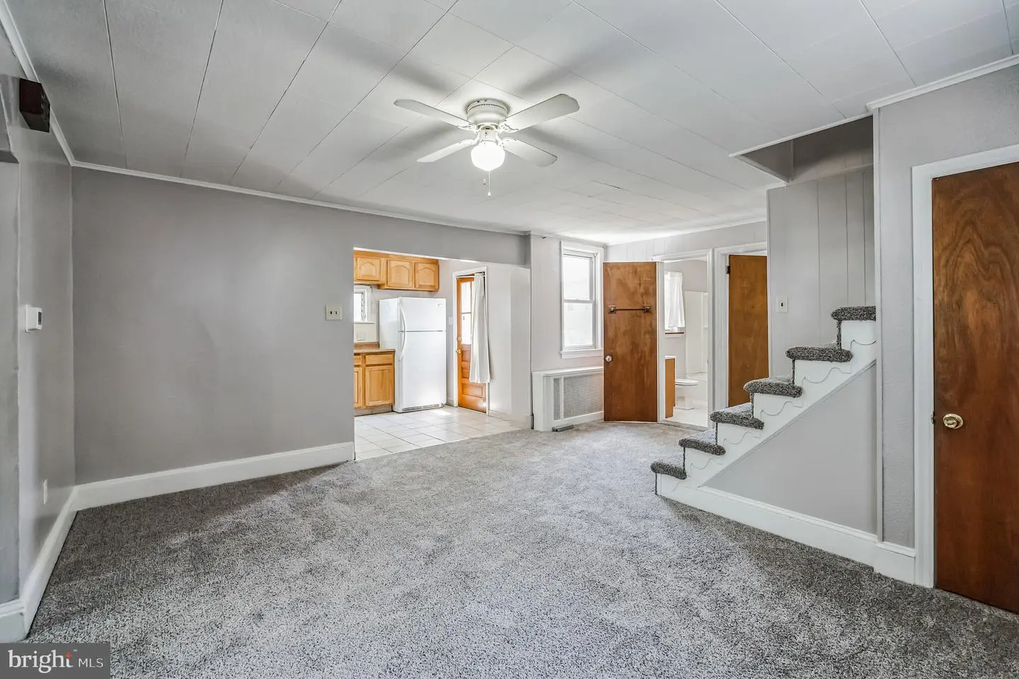 Carpeted living room with ceiling fan, stairs