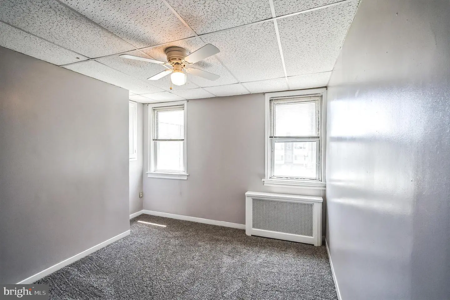 Empty carpeted bedroom with ceiling fan and windows