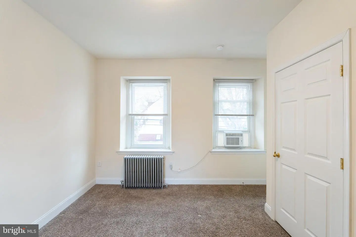 Empty bedroom with two windows, air conditioner, radiator